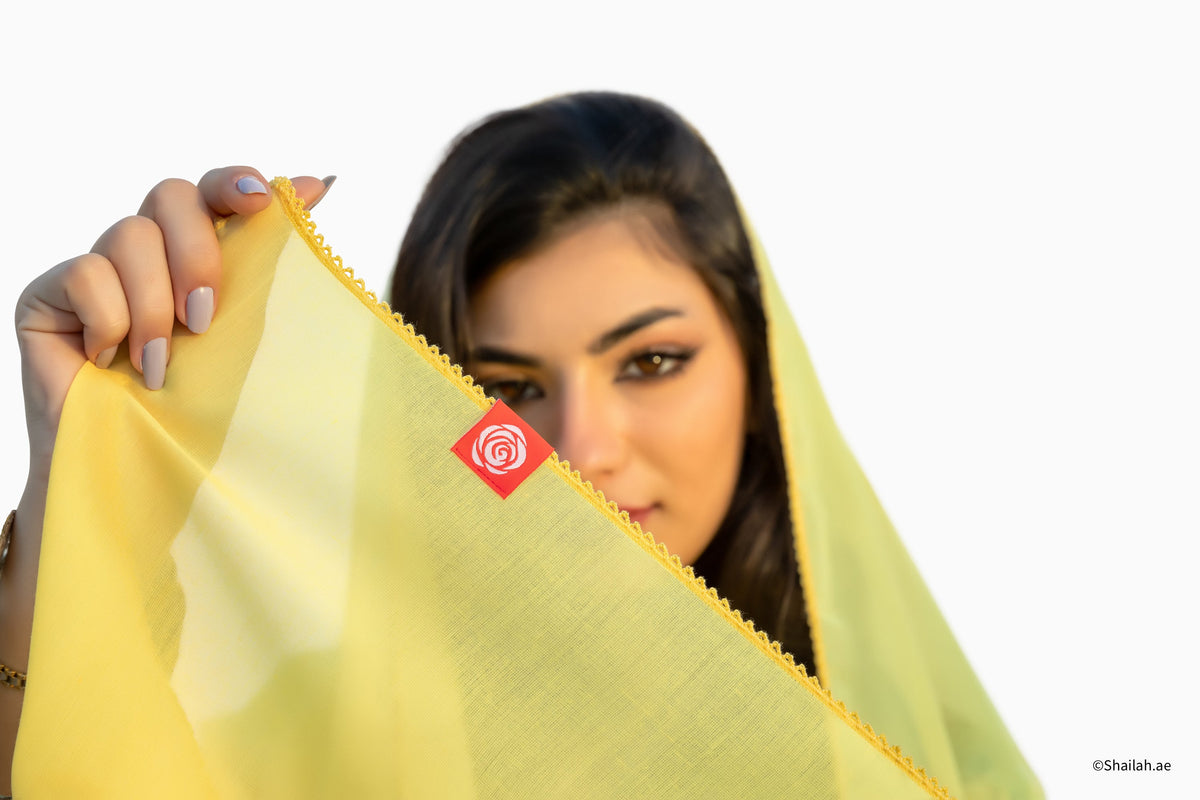 امرأة ترفع طرف شيلة سادة صفراء SD5-134 أمام خلفية بيضاء